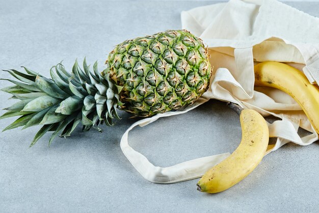 Ananas et banane mûrs dans un sac blanc sur une table bleue.