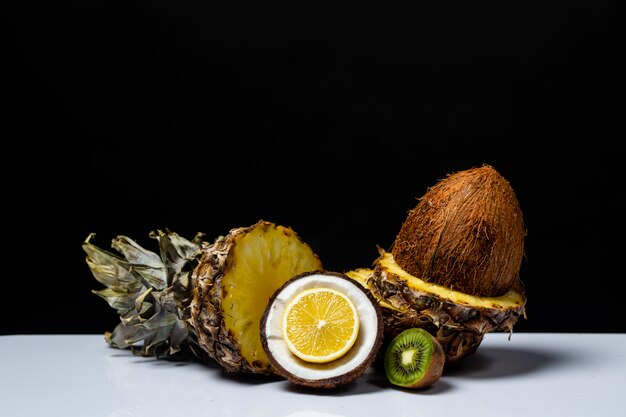 Ananas coco orange et kiwi coupés en deux sur une table sur fond noir