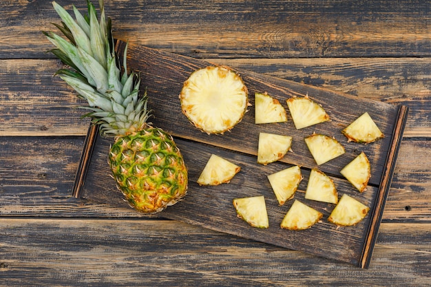 Ananas entier et tranché dans un morceau de bois sur une vieille surface de bois grunge. mise à plat.