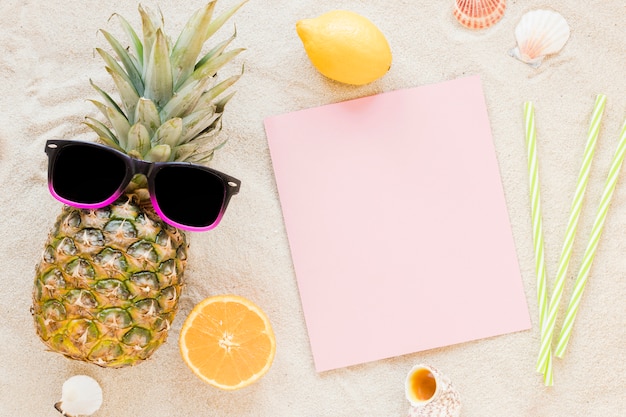 Ananas avec des lunettes de soleil et du papier sur le sable