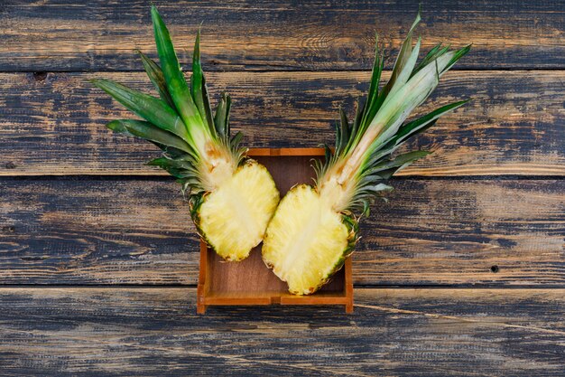 Ananas mûr coupé en deux dans une plaque de bois sur le vieux bois grunge, vue du dessus.