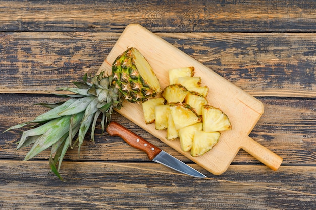 Photo gratuite ananas mûr en tranches dans une planche à découper avec un couteau à fruits vue de dessus sur une surface grunge bois