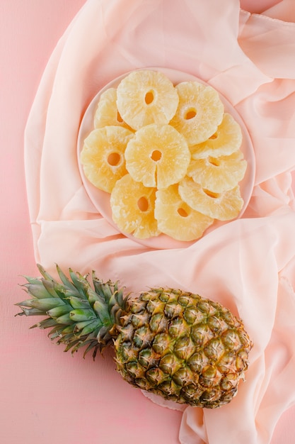 Ananas séchés à l'ananas frais dans une assiette sur surface rose et textile