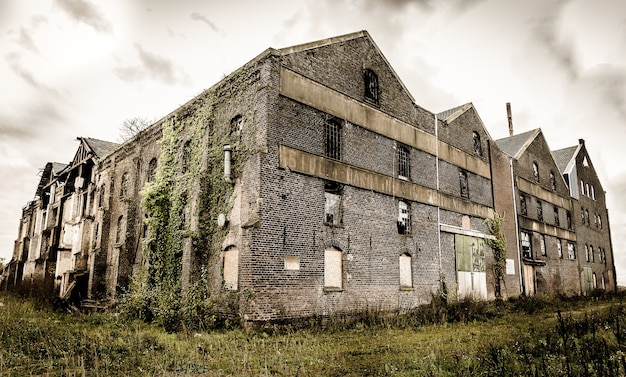Photo gratuite ancien bâtiment en pierre abandonné avec des fenêtres cassées sous le ciel nuageux sombre