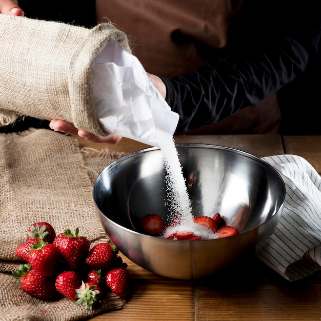 Angle élevé du chef ajoutant du sucre dans un bol de fraises