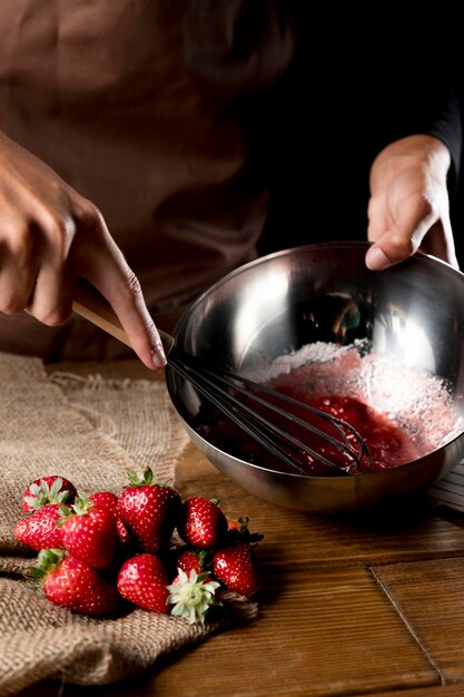 Angle élevé du chef fouettant les fraises dans un bol avec du sucre