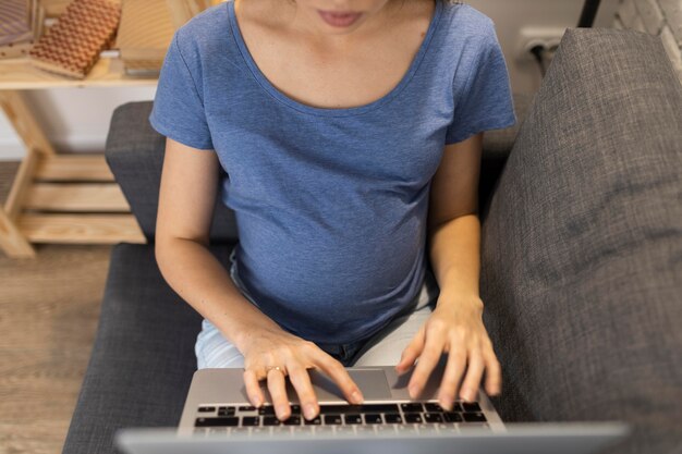 Angle élevé de femme d'affaires enceinte sur le canapé travaillant sur ordinateur portable