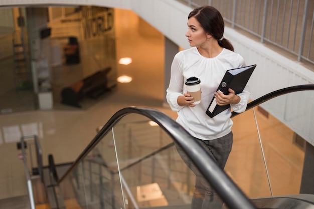 Angle élevé de femme d'affaires avec liant et café sur l'escalator