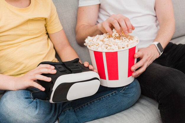 Angle élevé de l'homme et du garçon tenant un casque de réalité virtuelle et du pop-corn