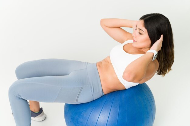 Angle élevé d'une jeune femme en vêtements de sport faisant des redressements assis sur un ballon d'exercice. Femme en forme active exerçant son abdomen tonique