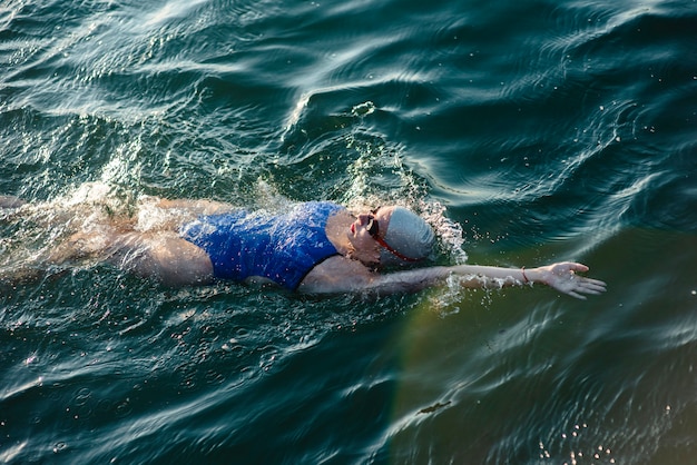 Angle élevé de nageuse avec bonnet et lunettes nageant dans l'eau