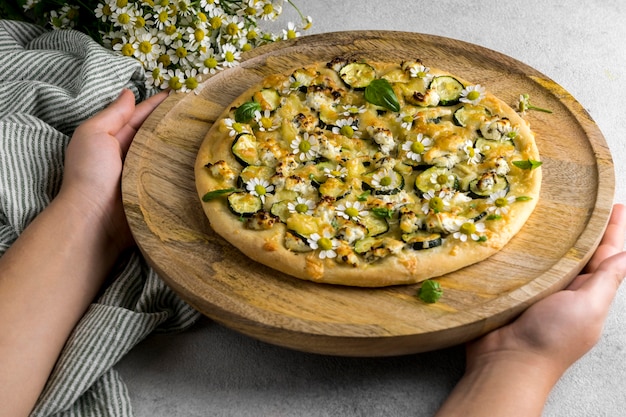 Photo gratuite angle élevé de personne tenant une délicieuse pizza cuite avec bouquet de fleurs de camomille