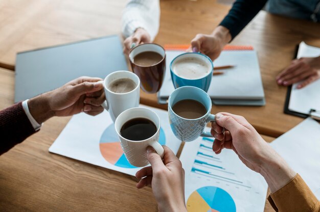 Angle élevé de personnes applaudissant avec des tasses à café pendant une réunion de bureau