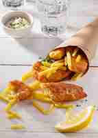 Photo gratuite angle élevé de poisson et frites en cornet de papier avec tranche de citron