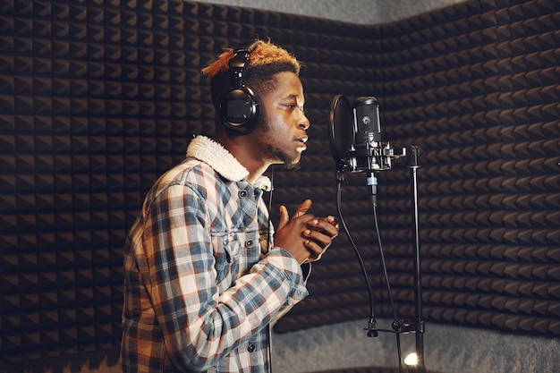 Animateur de radio faisant des gestes pendant l'enregistrement d'un podcast dans un studio de radio. L'homme africain répète dans un studio d'enregistrement.