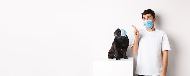 Photo gratuite animaux covid et concept de quarantaine jeune homme et chien noir portant des masques médicaux carlin et propriétaire loo