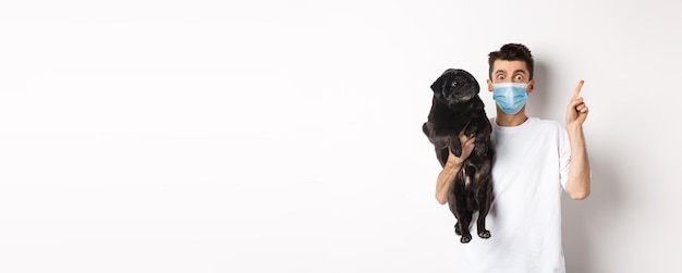 Animaux covid et concept de quarantaine jeune homme en masque médical tenant un mignon chien carlin noir à la recherche de ri