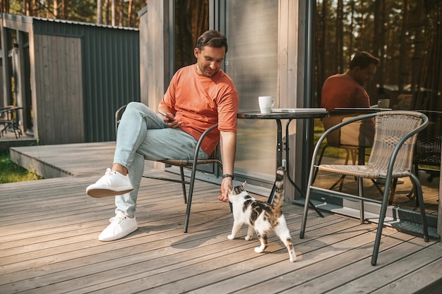 Animaux. Jeune homme assis dehors et caressant son chat