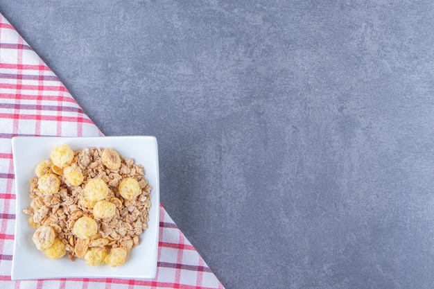 Anneau de maïs au miel avec muesli dans un bol sur un torchon, sur la table en marbre.