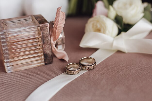 Anneaux de mariage avec gravure sur le ruban crémeux, le parfum et les fleurs blanches