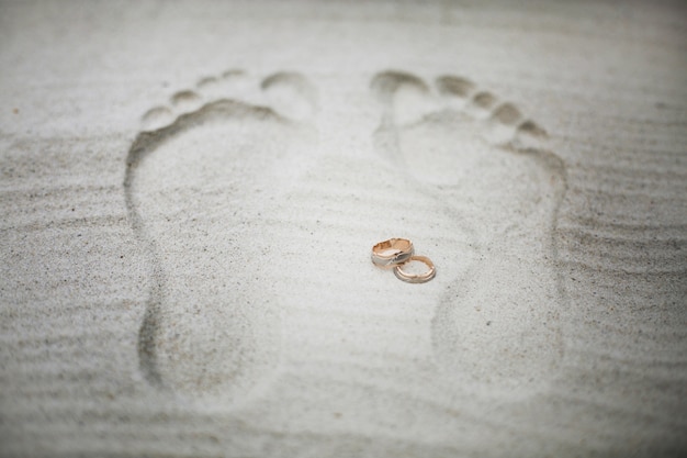 Les anneaux de mariage d&#39;or se trouvent entre les traces sur la plage