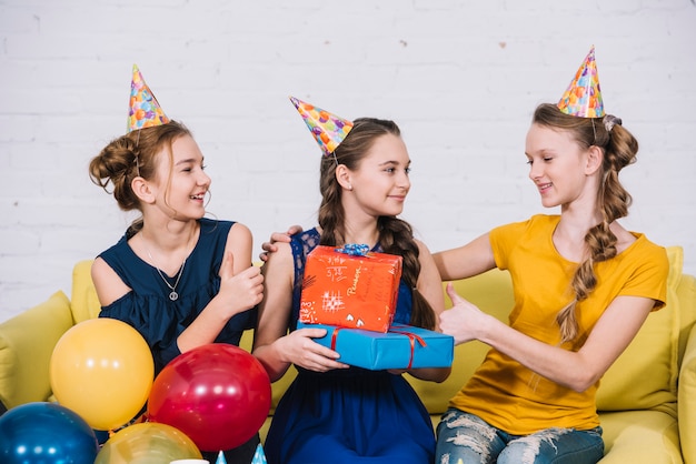 Anniversaire fille assise avec ses amies tenant des cadeaux dans la main