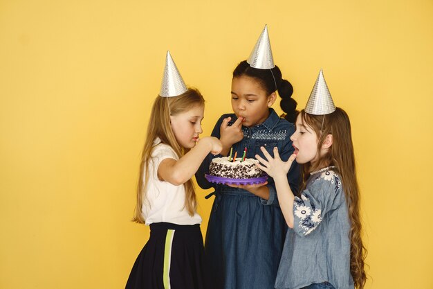 Anniversaire de petits enfants isolé sur mur jaune. enfants tenant un gâteau.