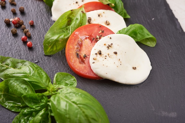 Antipasto de salade italienne fraîche appelée caprese avec mozzarella de bufflonne, tranches de tomates et basilic à l'huile d'olive. Ingrédients pour salade caprese végétarienne. Nourriture italienne. vue de dessus. Style rustique.