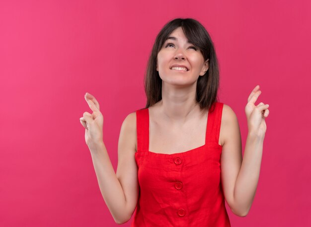 Anxieuse jeune fille de race blanche croisant les doigts les deux mains à la recherche sur fond rose isolé avec copie espace