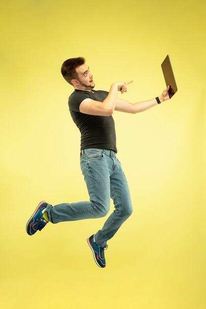 En apesanteur. Portrait en pied de l'homme sautant heureux avec des gadgets isolés sur fond jaune