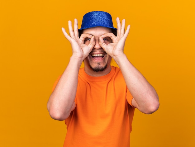 Appareil photo joyeux à la recherche d'un jeune homme portant un chapeau de fête montrant un geste de regard