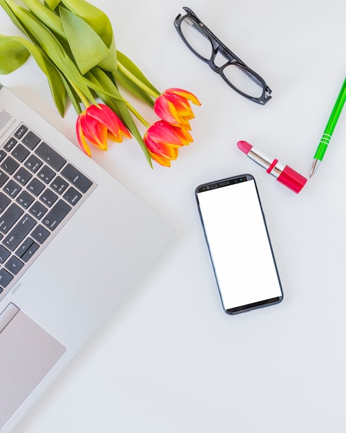 Appareils électroniques à proximité des fleurs, du rouge à lèvres et des lunettes