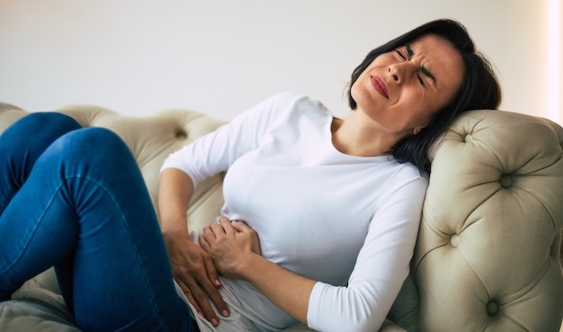 Appendicite. une jeune femme adulte est allongée sur un canapé et se tient le ventre tout en souffrant d'une douleur insupportable.