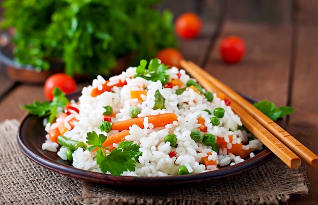 Appétissant riz sain avec des légumes en plaque blanche sur une table en bois.