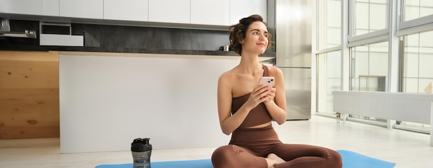 Photo gratuite application de sport et de bien-être jeune femme athlète assise sur le sol à la maison avec un smartphone faisant du yoga