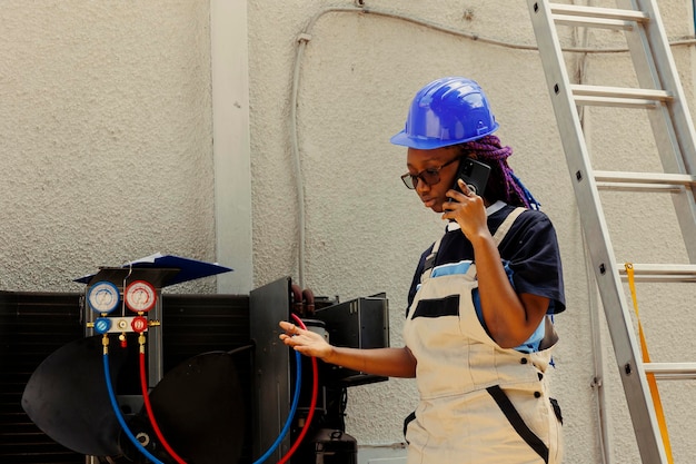 Photo gratuite un apprenti afro-américain appelle le responsable pour se renseigner sur les composants nécessaires du condenseur qui doivent être remplacés. électricien vérifiant le plan de maintenance après avoir résolu de mauvais problèmes de câblage