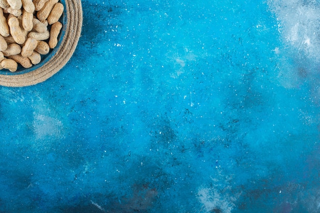 Arachides en coque dans une assiette en bois sur dessous de plat sur la surface bleue