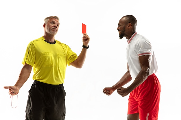 Arbitre montrant un carton rouge à un joueur de football ou de football afro-américain mécontent tout en jouant isolé sur un mur blanc. Concept de sport, violation des règles, questions controversées, émotions.