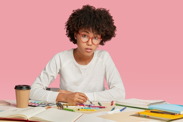 L'architecte a une coiffure afro, travaille sur le projet de conception, dessine des images dans un cahier ressemble sérieusement, porte des lunettes