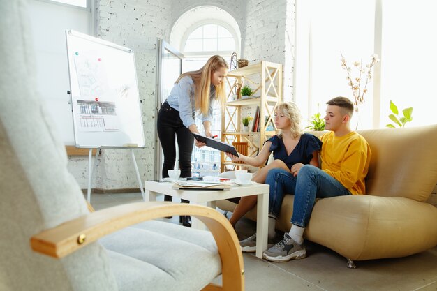 Architecte d'intérieur travaillant avec un jeune couple. Belle famille et designer professionnel ou architecte discutant du concept de futur intérieur, travaillant avec une palette de couleurs, des dessins de pièce dans un bureau moderne.