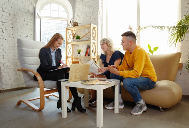 Architecte d'intérieur travaillant avec un jeune couple. Belle famille et designer professionnel ou architecte discutant du concept de futur intérieur, travaillant avec une palette de couleurs, des dessins de pièce dans un bureau moderne.