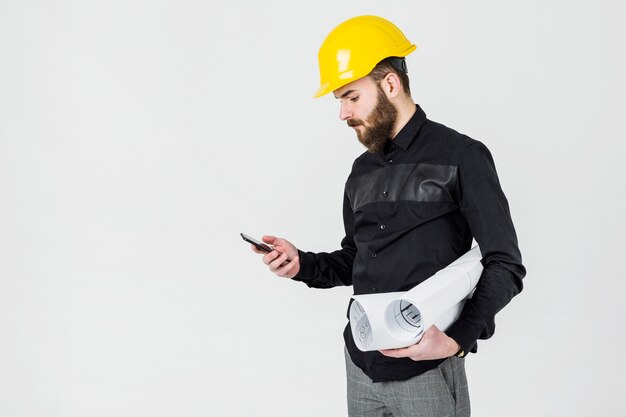 Un architecte mâle portant un casque jaune regardant smartphone