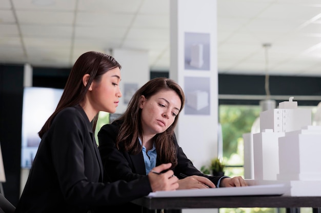 Architectes travaillant avec des plans, discutant de la construction d'un modèle imprimé en 3d, regardant un prototype architectural dans un espace de coworking. Employés dans un bureau d'architecture, employés d'une agence immobilière