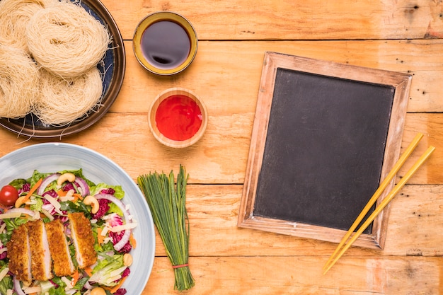 Ardoise vierge avec des baguettes et de la nourriture traditionnelle thaïlandaise sur une table en bois