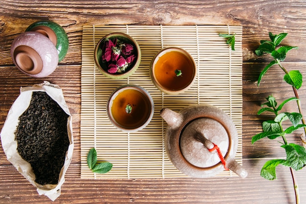 Arrangement de la cérémonie du thé asiatique traditionnelle avec des pétales de rose et une brindille de menthe sur un bureau en bois