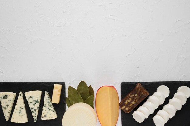 Arrangement de divers fromages sur une ardoise noire avec des feuilles de laurier au coin de la surface blanche