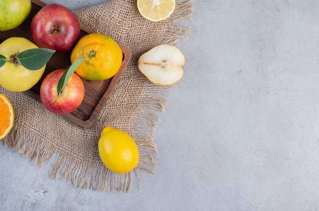 Un arrangement de divers fruits sur une planche de bois et un morceau de tissu sur fond de marbre.