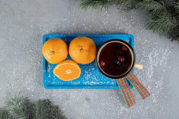 Arrangement festif avec une tasse en métal et des oranges sur une table en marbre.