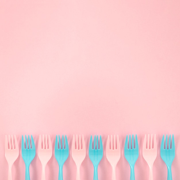 Photo gratuite arrangement de fourchettes en plastique coloré sur fond rose