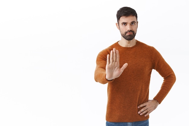 Arrêtez assez de ça. Portrait d'un bel homme barbu confiant, tendant la main dans l'interdiction, désapprouve le comportement, interdit l'action, ne sors pas pendant la quarantaine, mur blanc